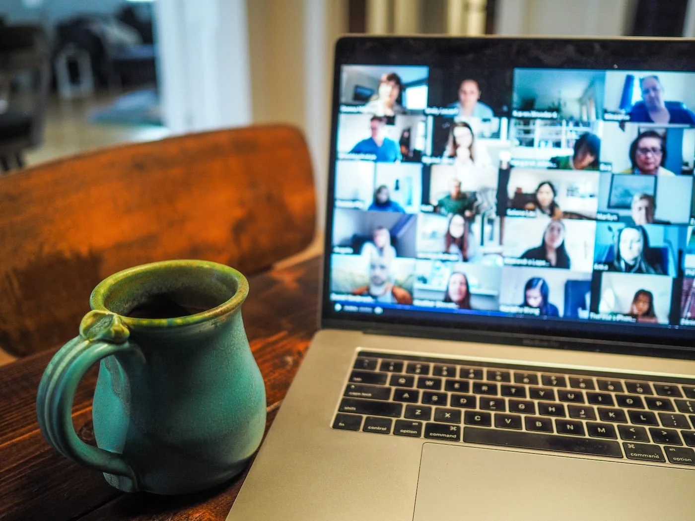 A laptop showing a video call beside a coffee mug