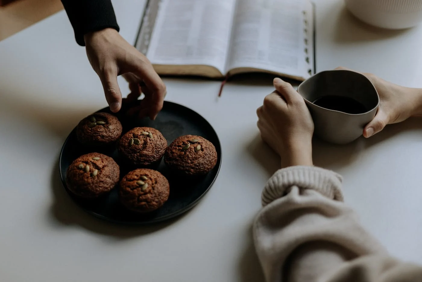Hands around coffee mugs and an open Bible at a small group